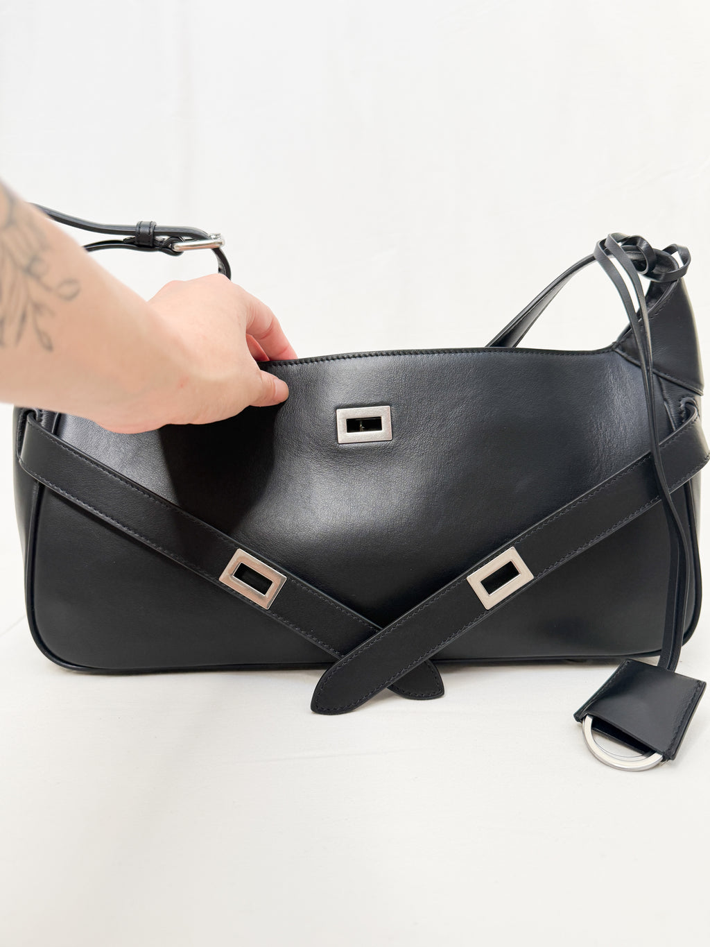 Black leather handbag with silver buckles held by a hand on a white background
