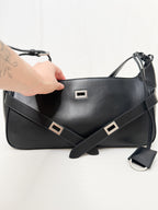 Black leather handbag with silver buckles held by a hand on a white background