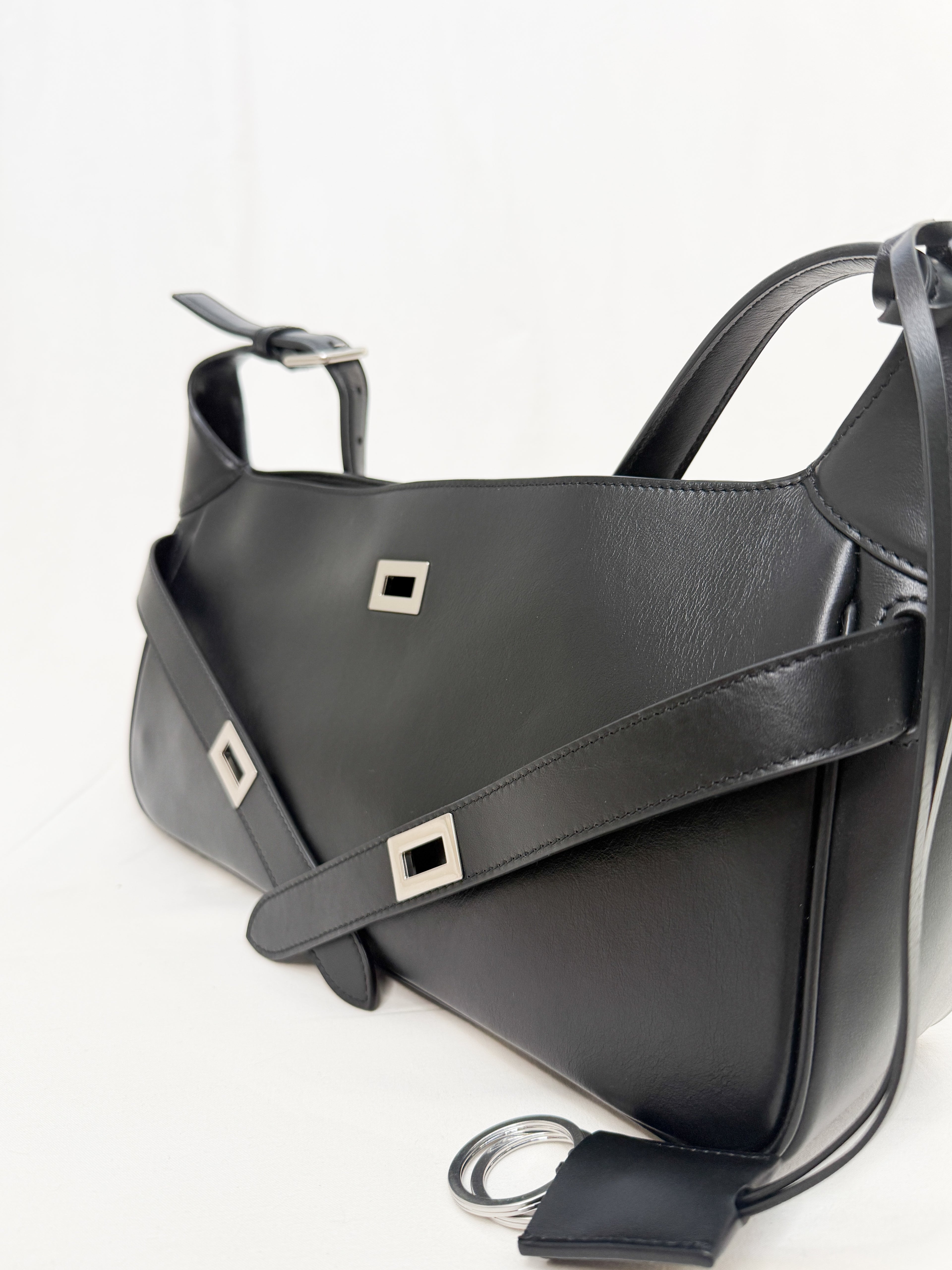 Black leather handbag with silver buckles on a white background
