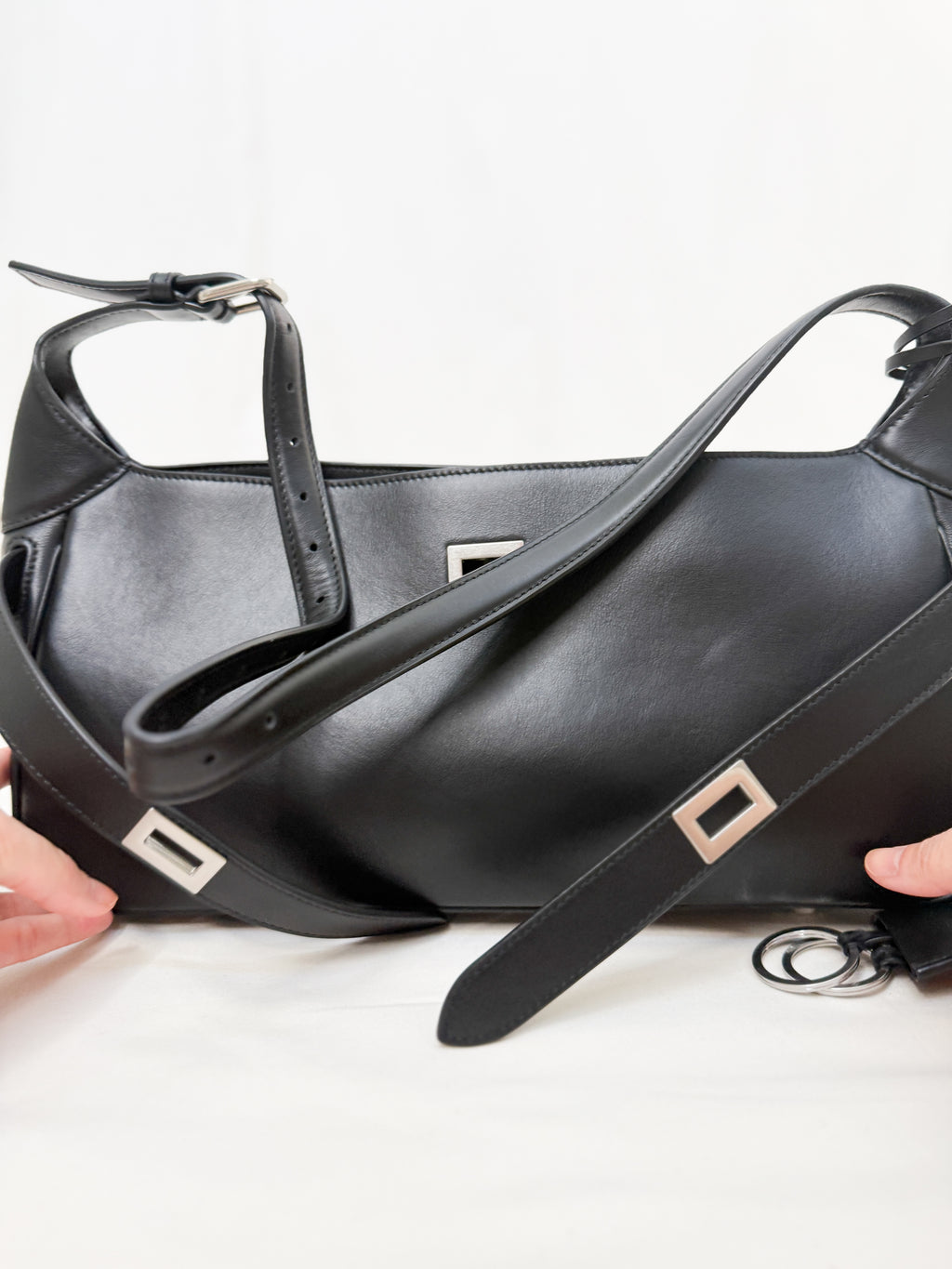 Black leather handbag with a strap held by hands on a white background
