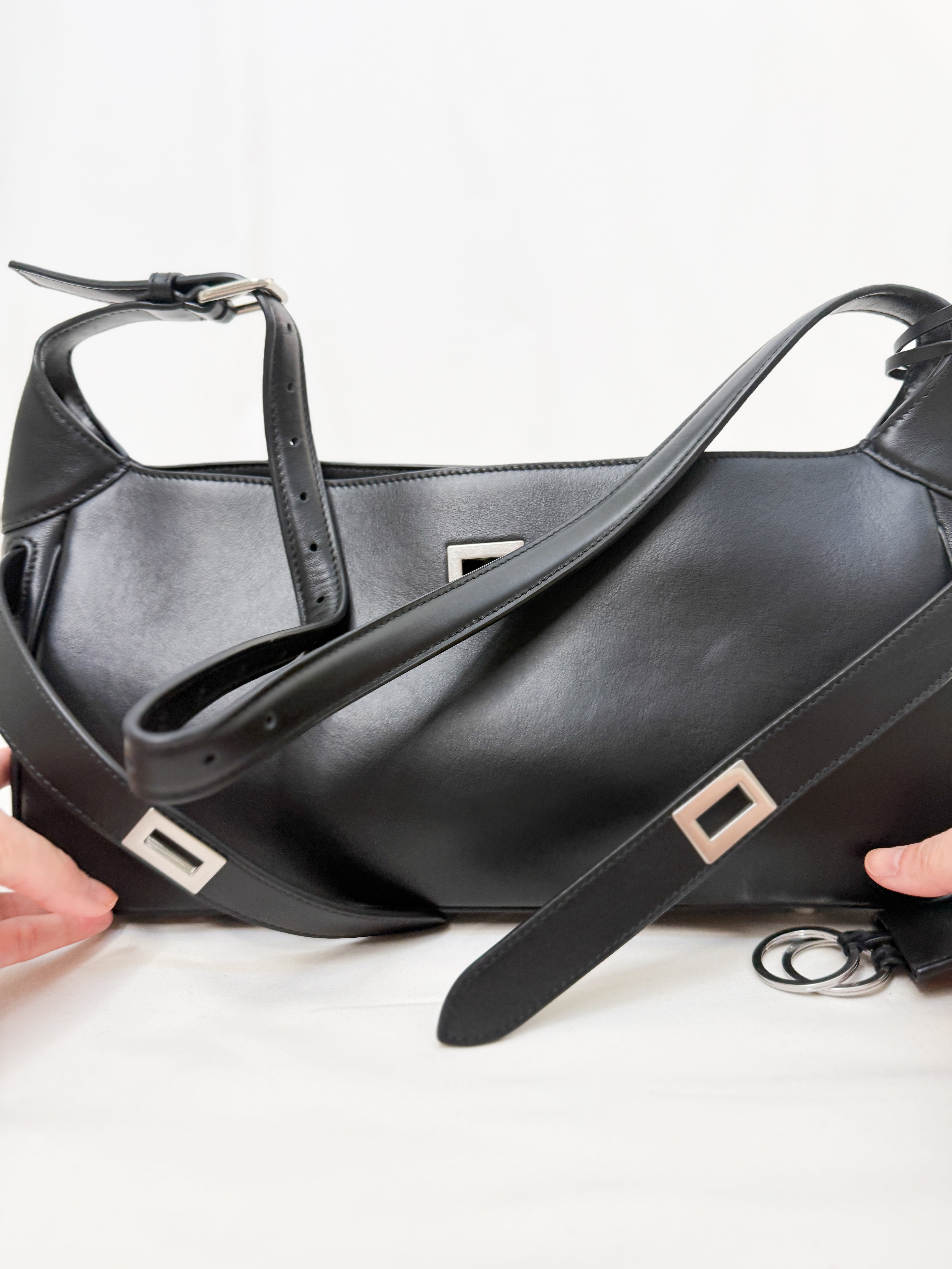 Black leather handbag with a strap held by hands on a white background