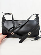 Black handbag with a strap held by a hand on a white background