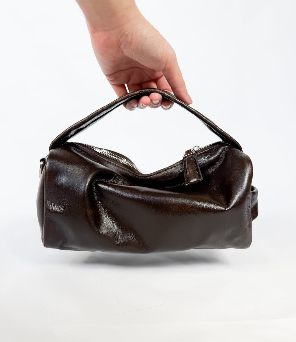 Brown leather handbag held by a hand on a white background