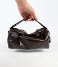 Brown leather handbag held by a hand on a white background