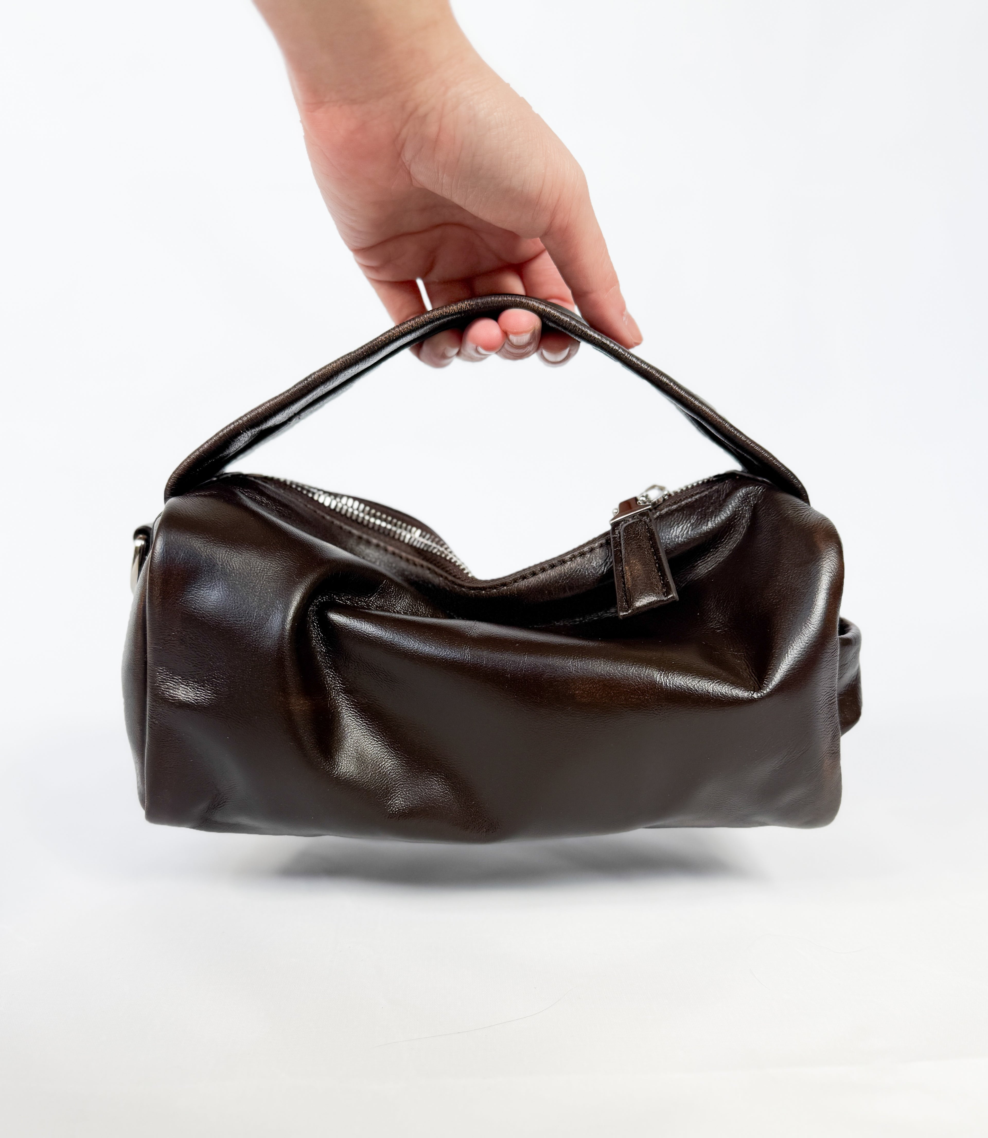 Brown leather handbag held by a hand on a white background